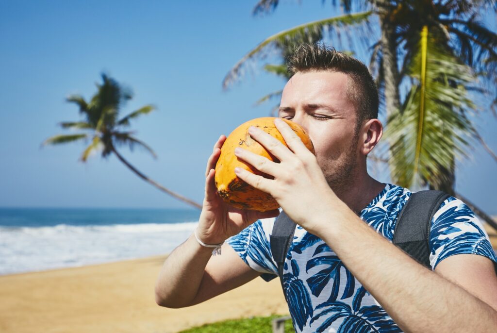 Thirsty young man drinking coconut water. Relaxation on the sand beach. Sri Lanka